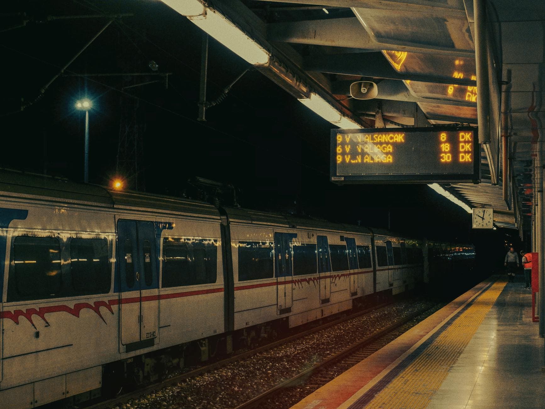 A night time view of the İzmir metro station with a stationary train and an illuminated signboard.