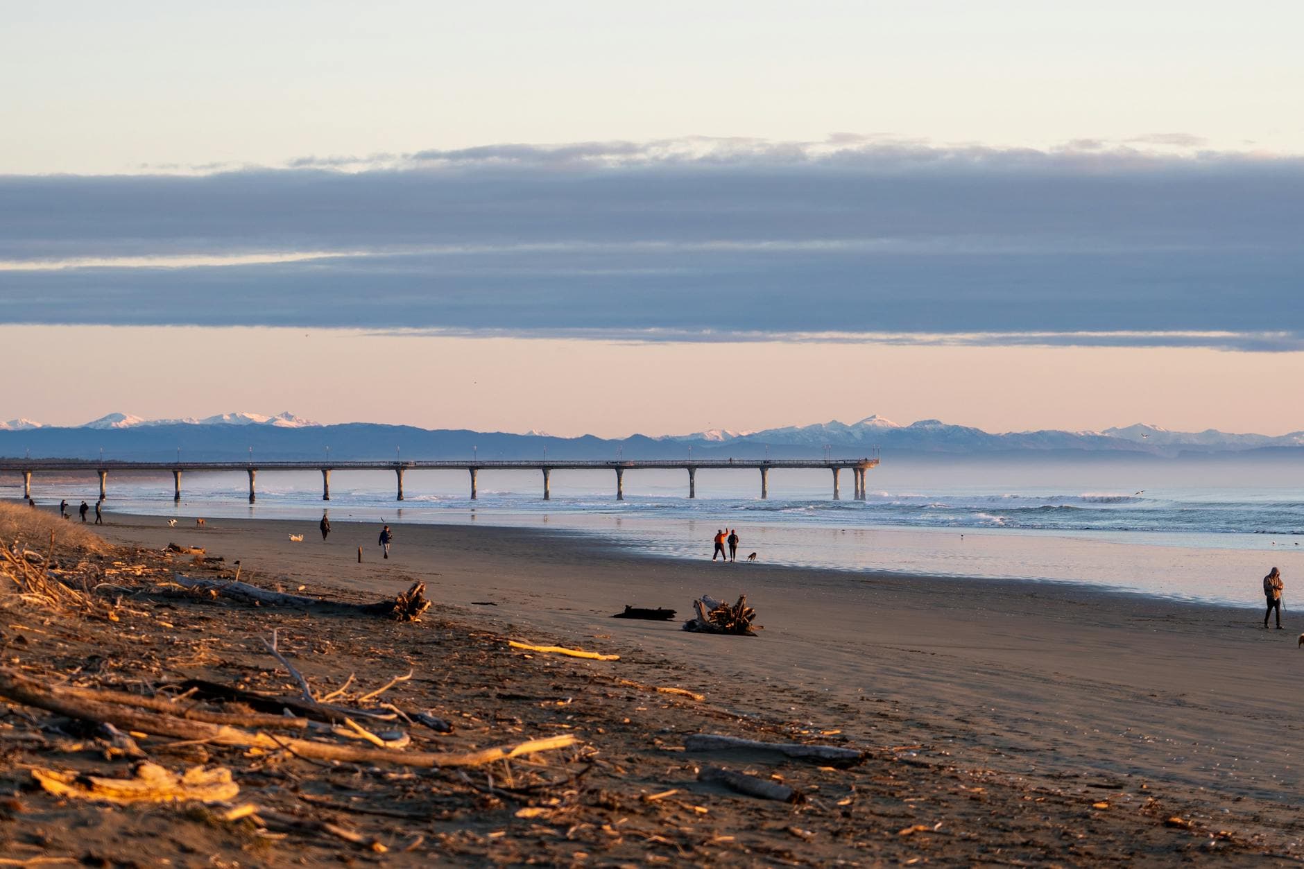 Scenic view of New Brighton Beach at sunset with a pier and distant mountains in Christchurch, NZ.