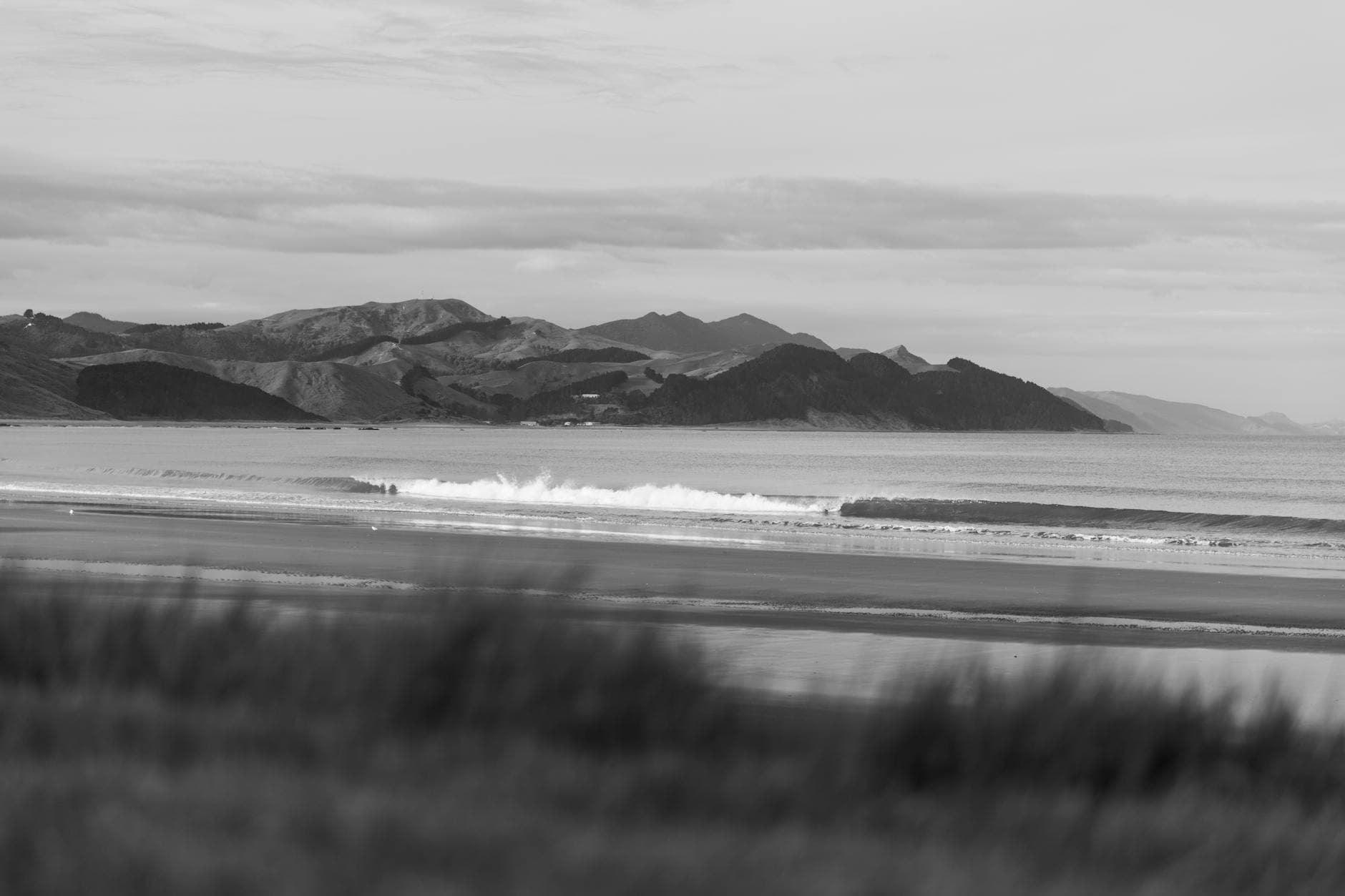 Black and white view of Castlepoint Beach with mountains in New Zealand's North Island.