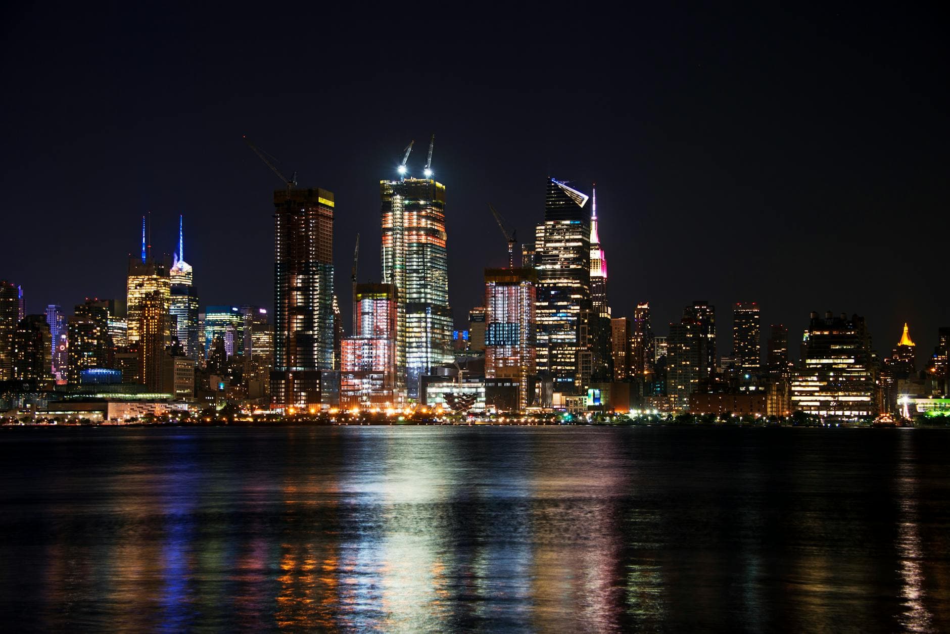 Stunning view of New York City's illuminated skyline with reflections on the Hudson River at night.