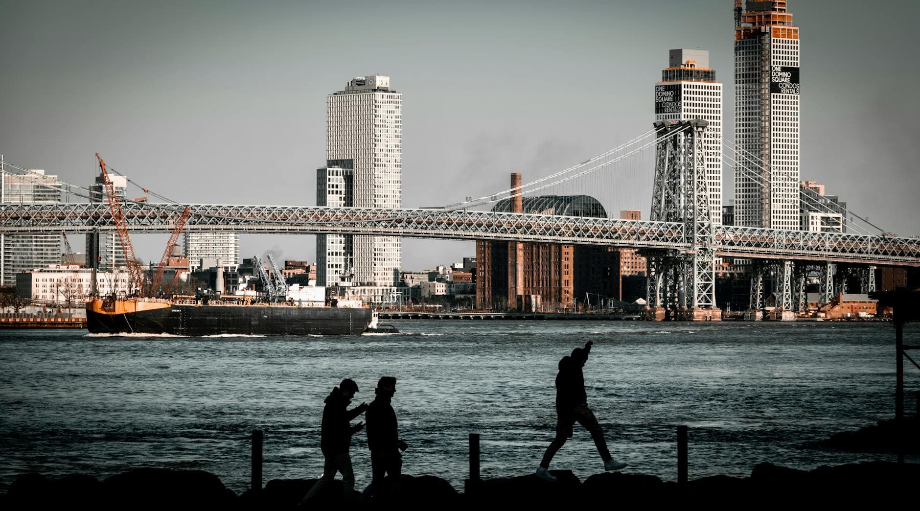 Silhouette of people walking by the Williamsburg Bridge and city skyline in New York City.