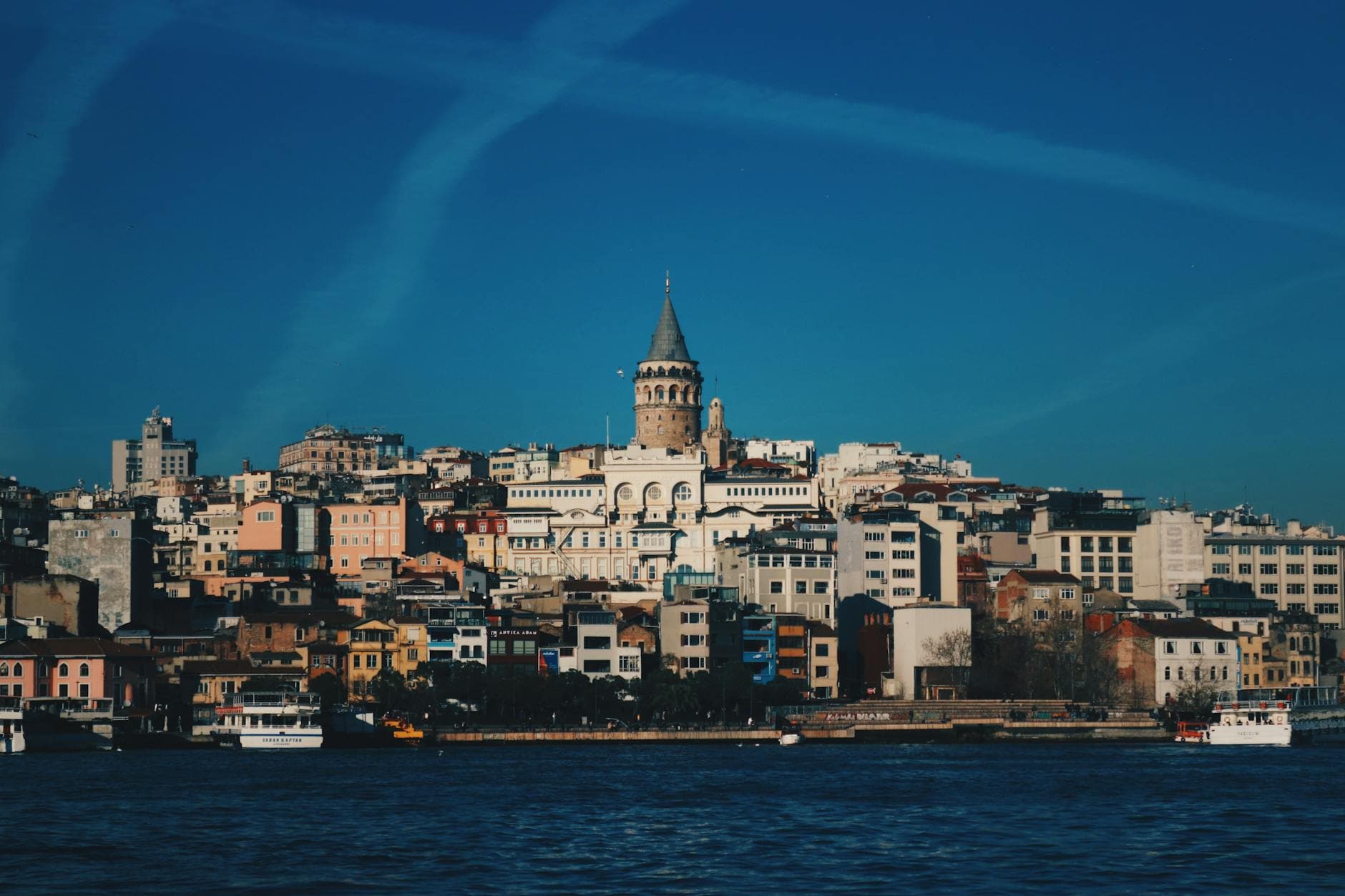 View of Galata Tower rising above the colorful cityscape of Istanbul, near the sea.
