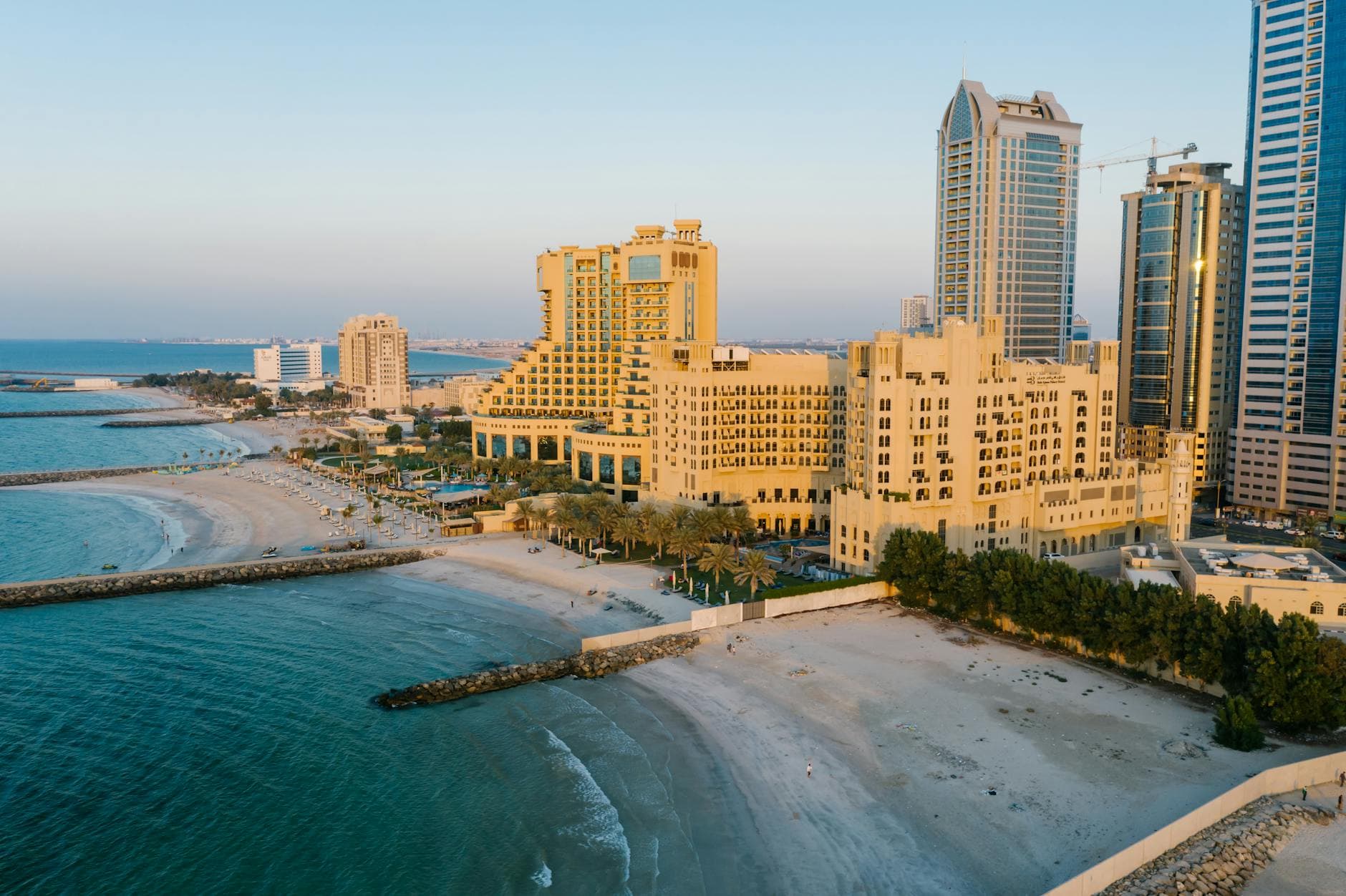 A stunning aerial view of Ajman's coastline with towering hotels and the tranquil beach at sunset.