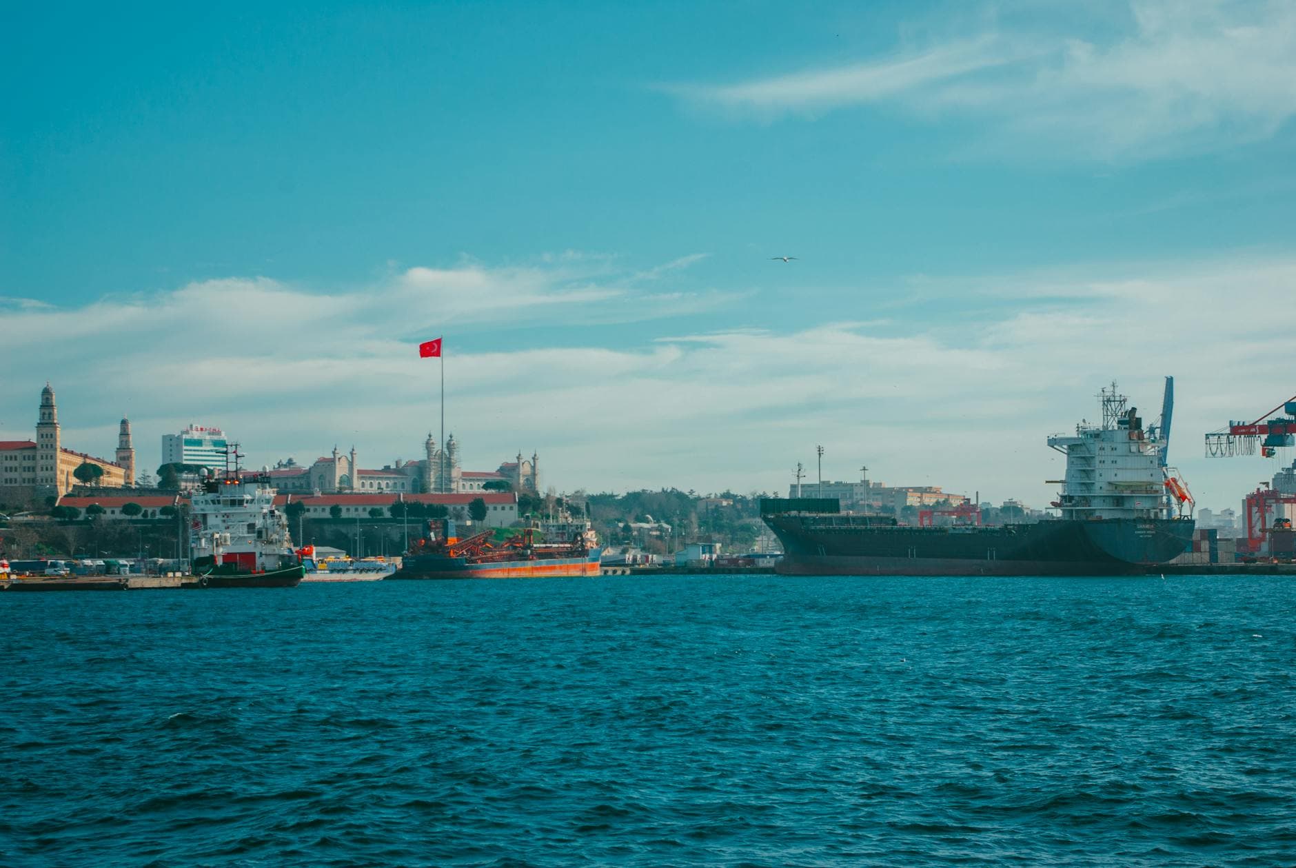 Turkish harbor with ships and skyline, featuring clear skies and a national flag.