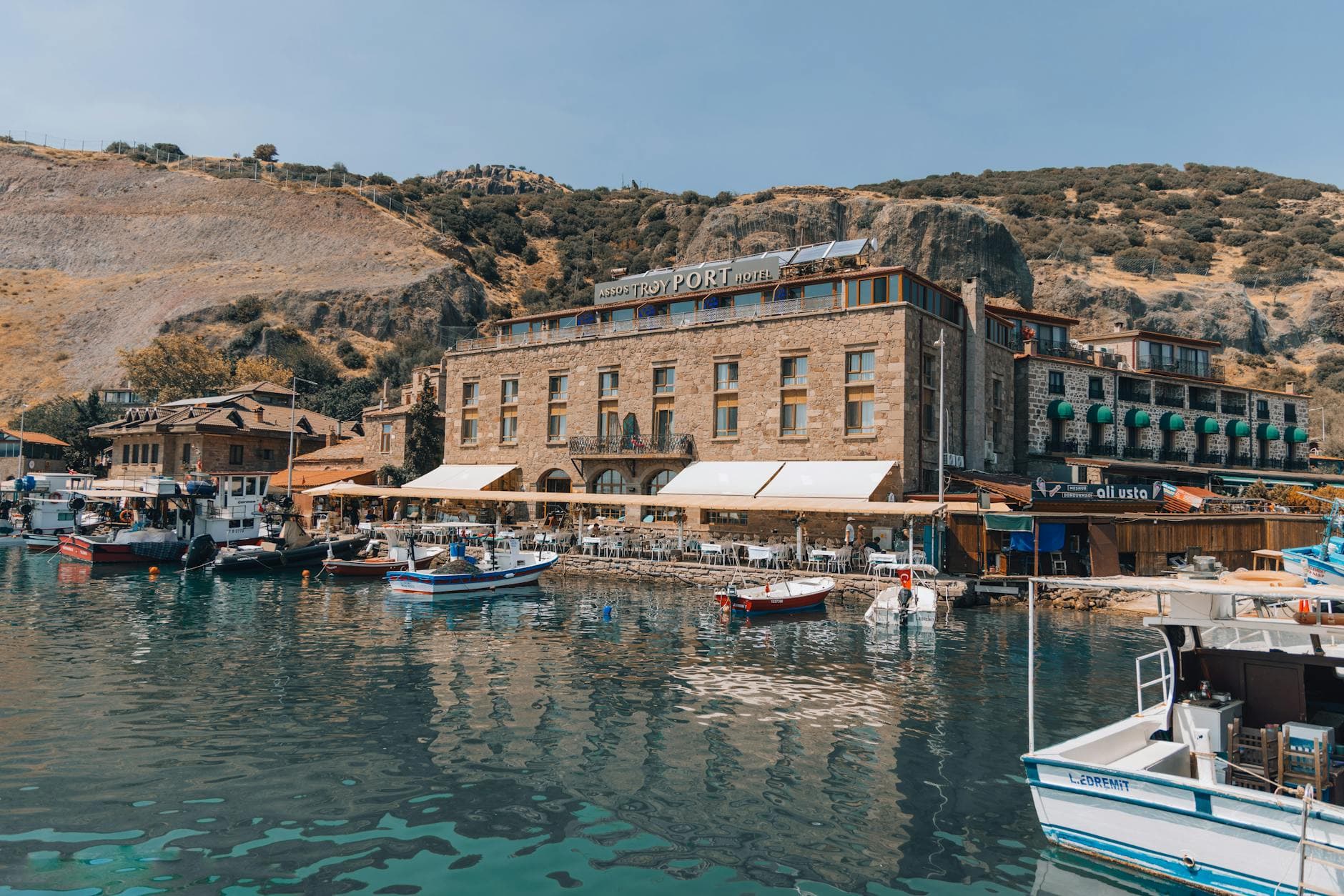 Charming boutique hotel by the waterfront with boats and rocky hills in the backdrop.