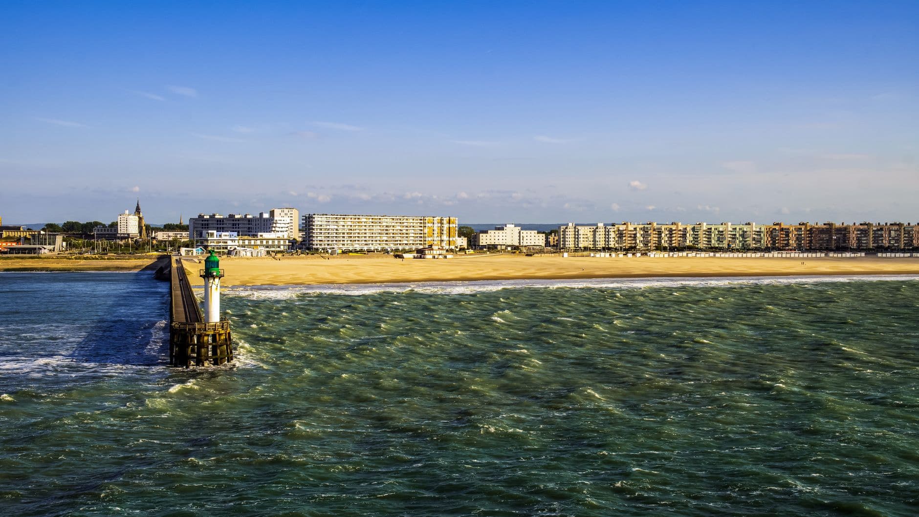 Vibrant seaside view of Calais, France with pier, sandy beach, and cityscape.