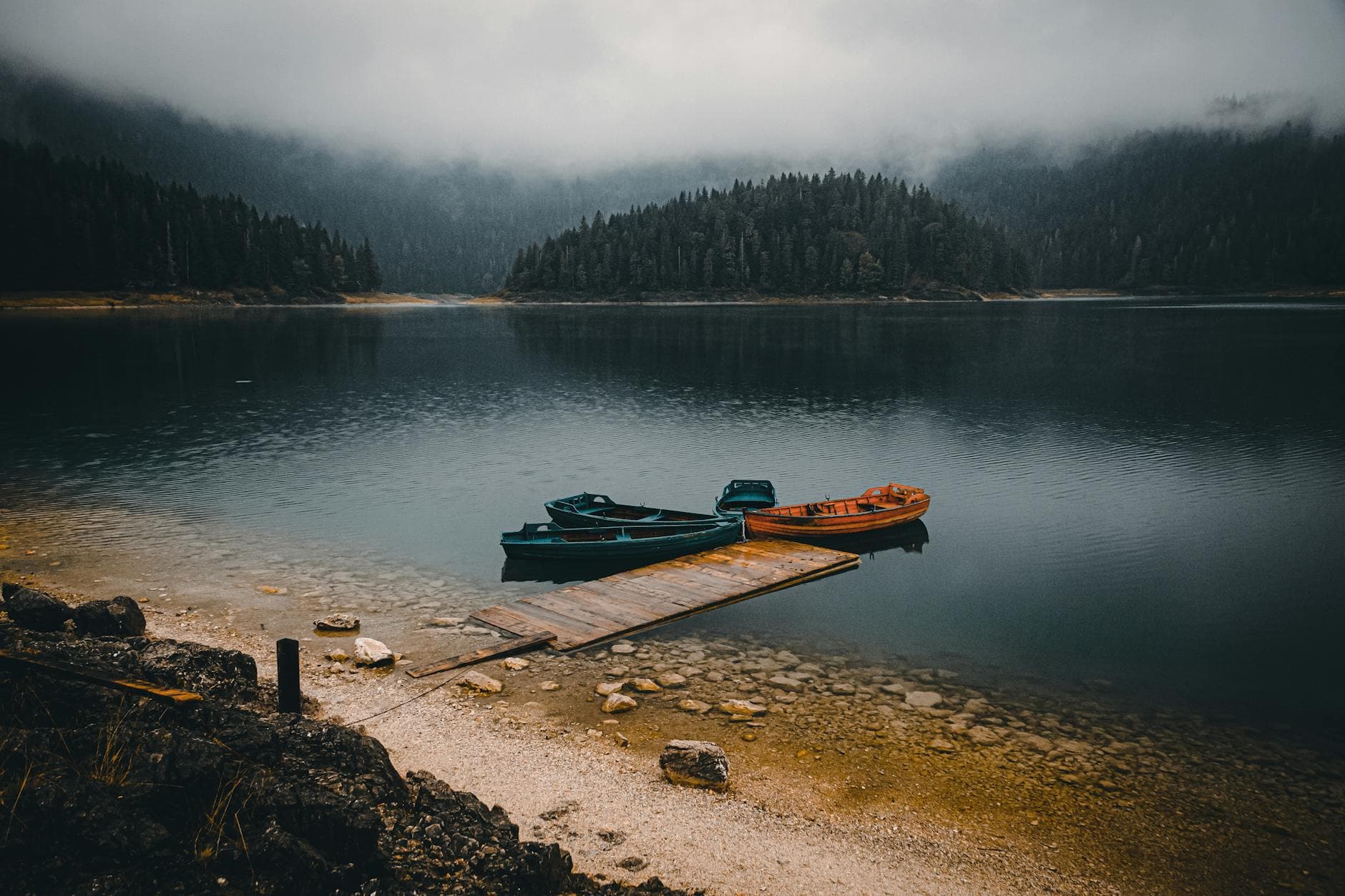 Tranquil view of wooden boats on a misty lake surrounded by forested mountains in Montenegro.