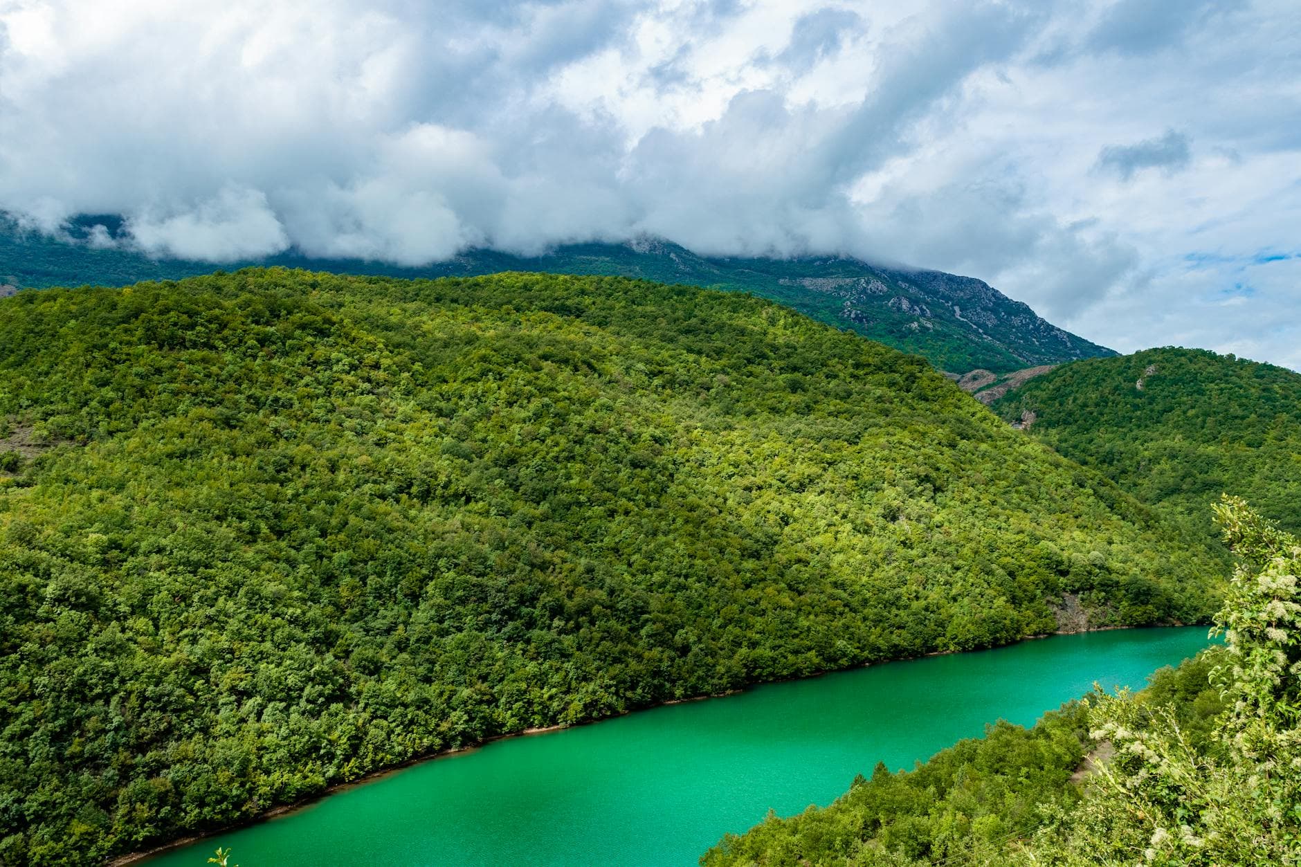 A stunning view of lush green mountains and a turquoise lake under a cloudy sky in Žabljak, Montenegro.