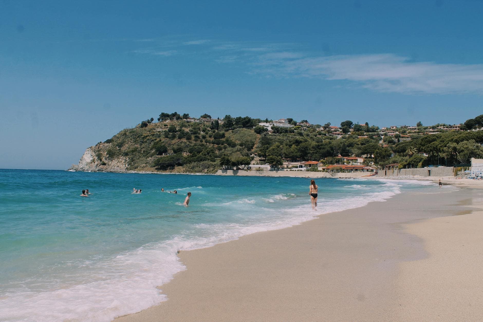 Beautiful beach in Celico, Italy with clear blue waters and distant hillside view.