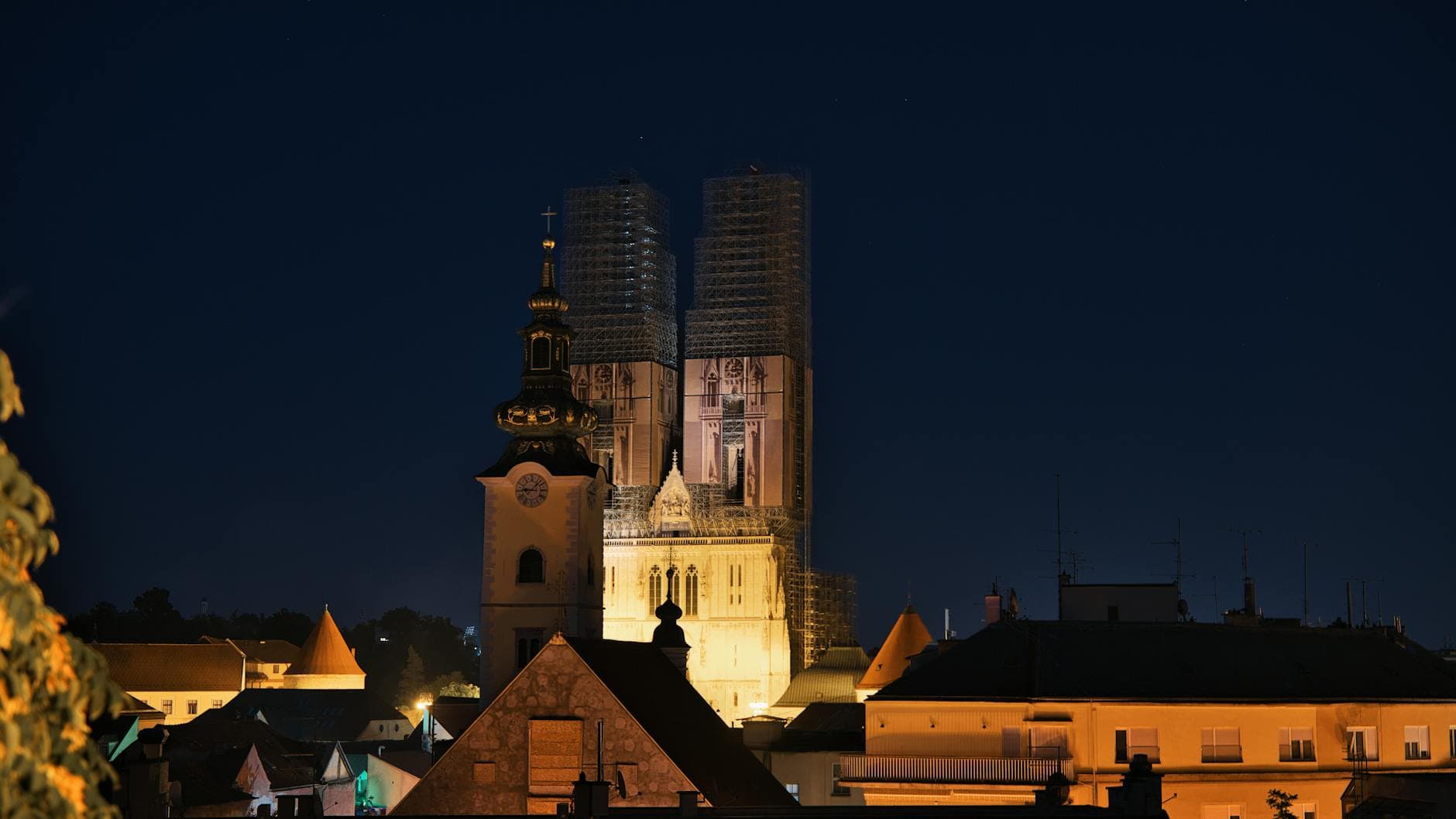 Night view of the illuminated Zagreb Cathedral, surrounded by rooftops.