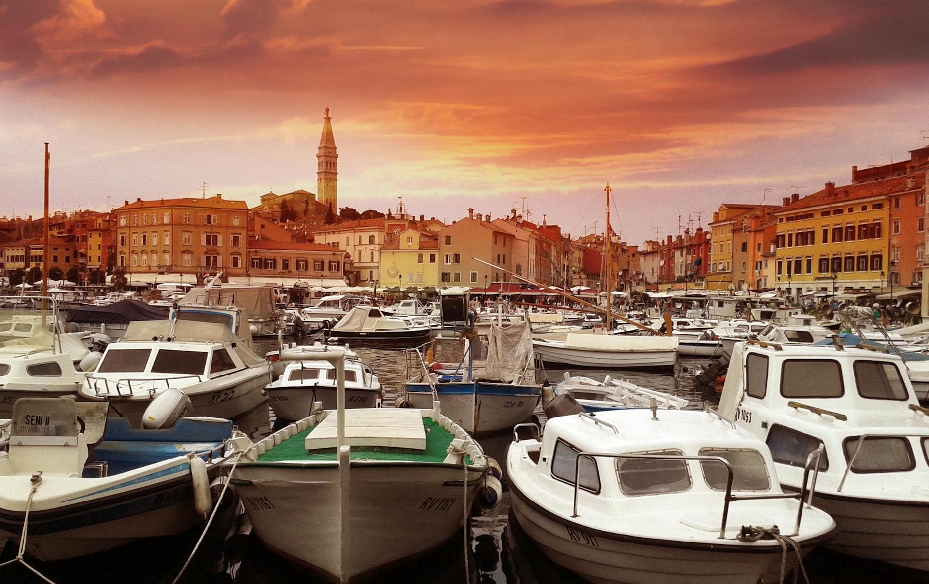 Vibrant sunset over Rovinj harbor with moored boats and historic town skyline.