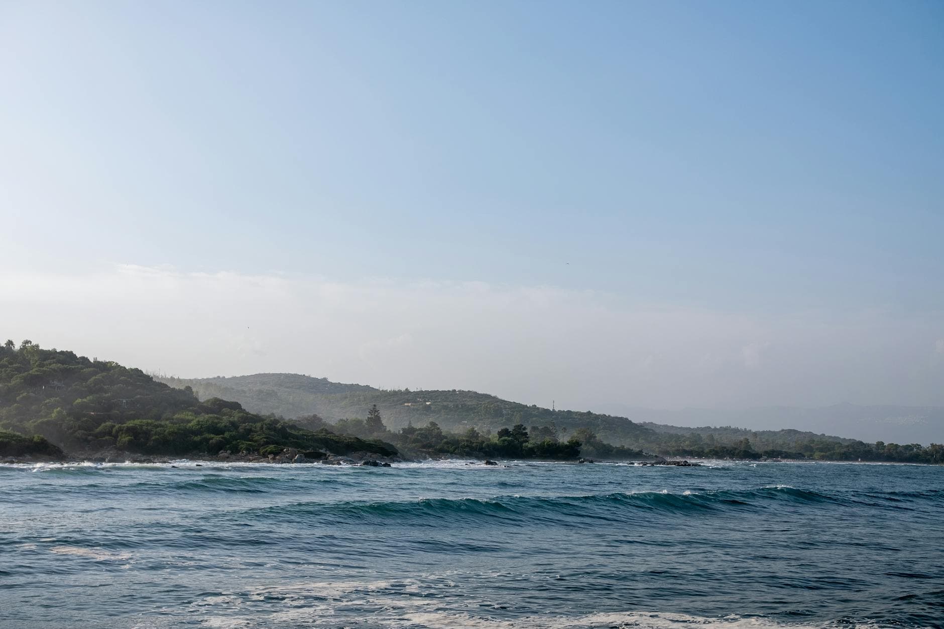A serene coastal view in Sardinia, Italy, showcasing the azure sea and lush greenery under a clear sky.