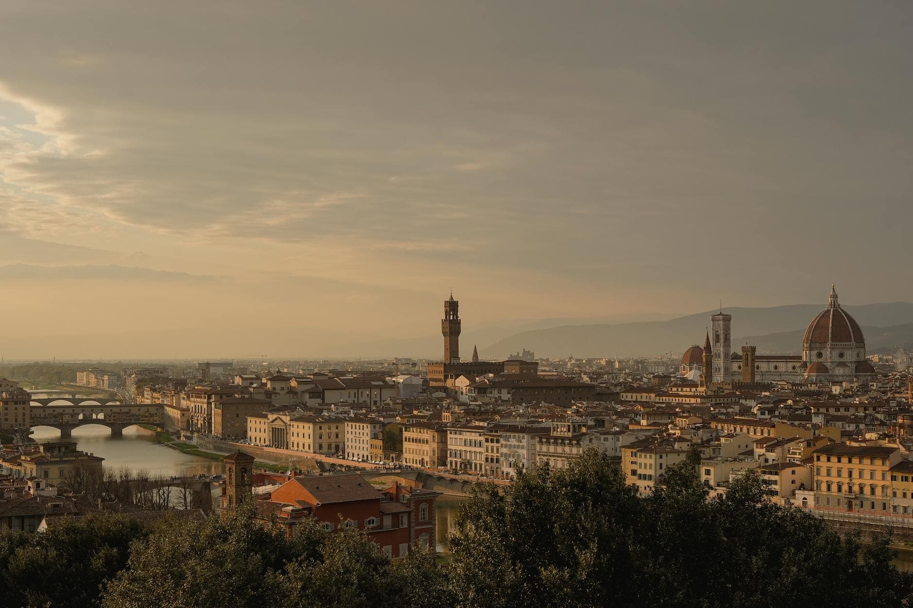 A picturesque view of Florence, Italy at sunset, featuring the iconic Duomo and historic bridges.