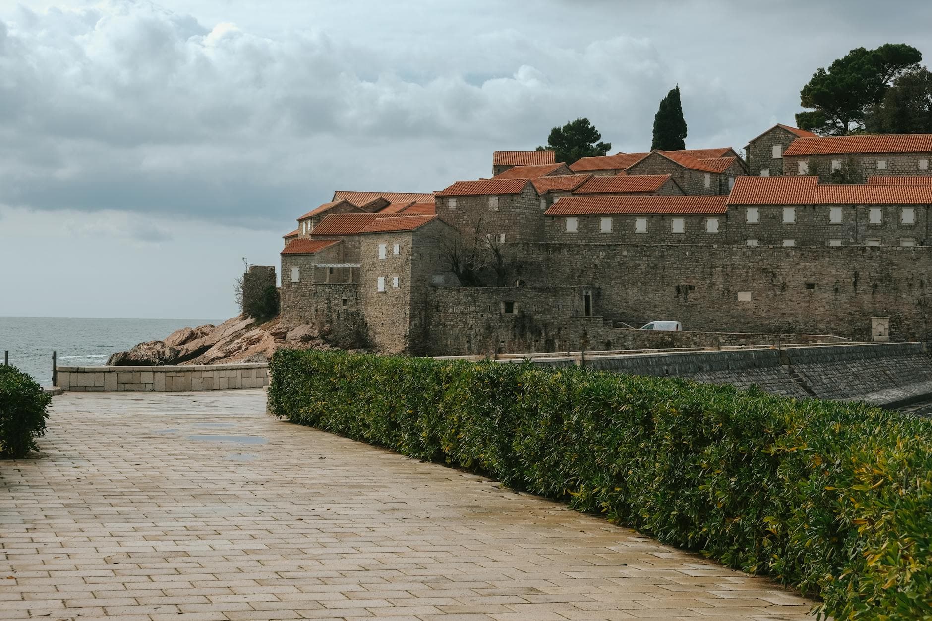 Serene view of a historic coastal castle with stone walls and red roofs under a cloudy sky by the sea.