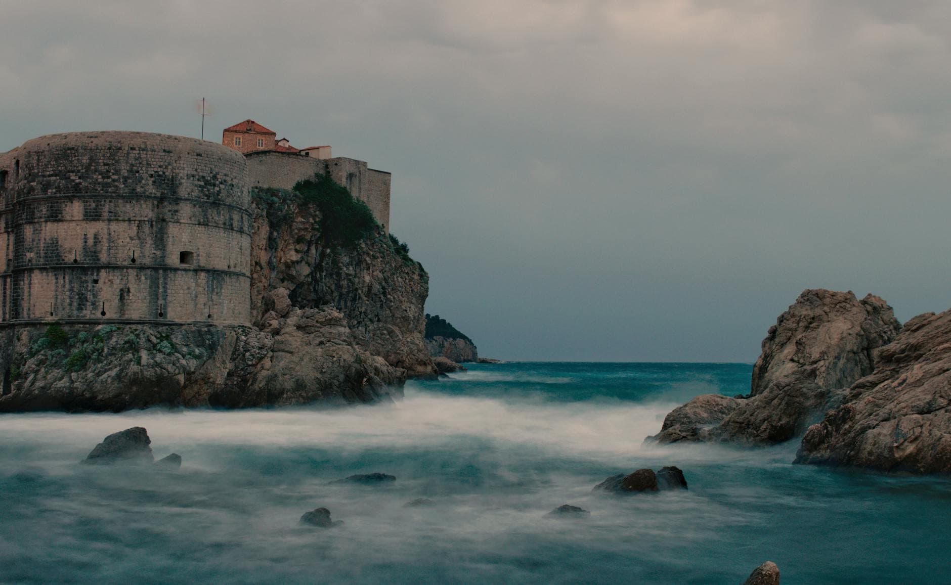 A stunning view of a historic fortress perched on a rocky coastline under cloudy skies.