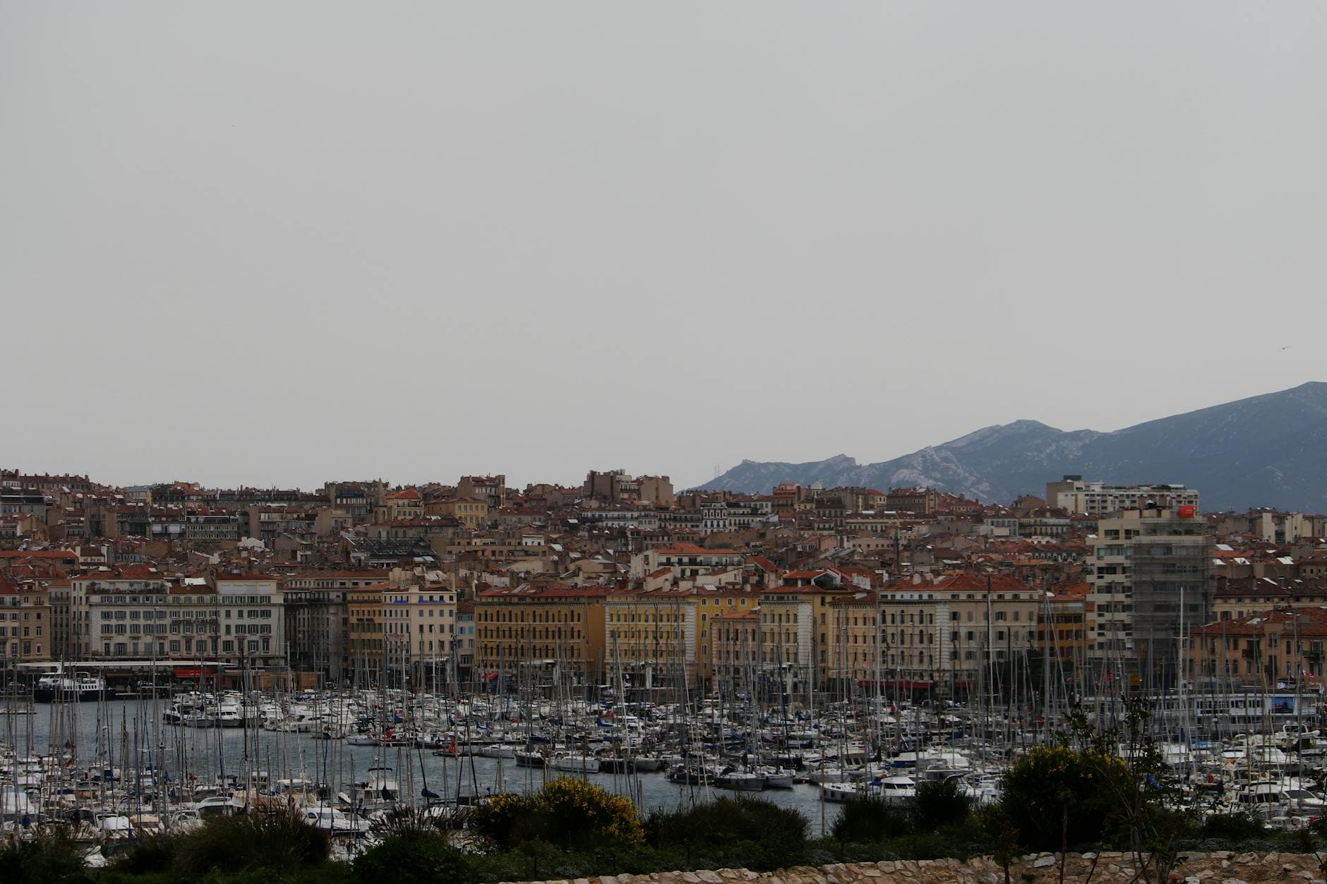 Scenic view of Marseille harbor with historic buildings and moored boats under a cloudy sky.