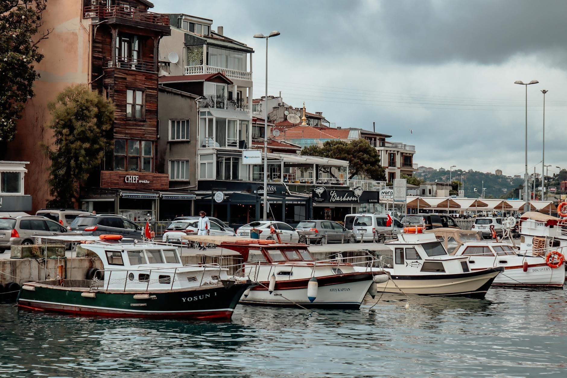 Coastal harbor view with moored motorboats and historic buildings under overcast skies.