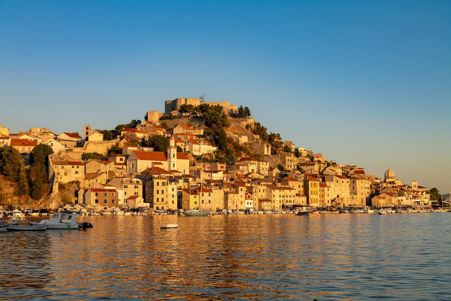 A picturesque view of Šibenik's historic waterfront at sunset, reflecting golden hues.