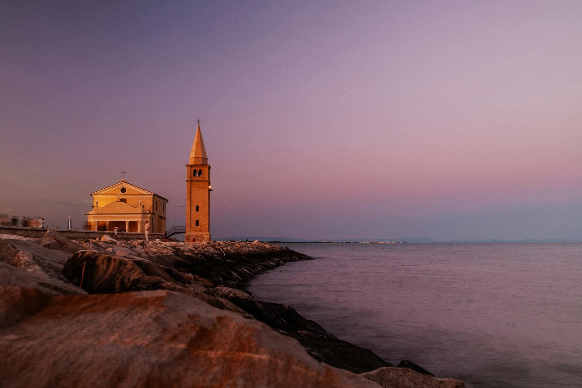Captivating sunset view of the historic church in Caorle, Italy, with colorful skies reflecting on the water.