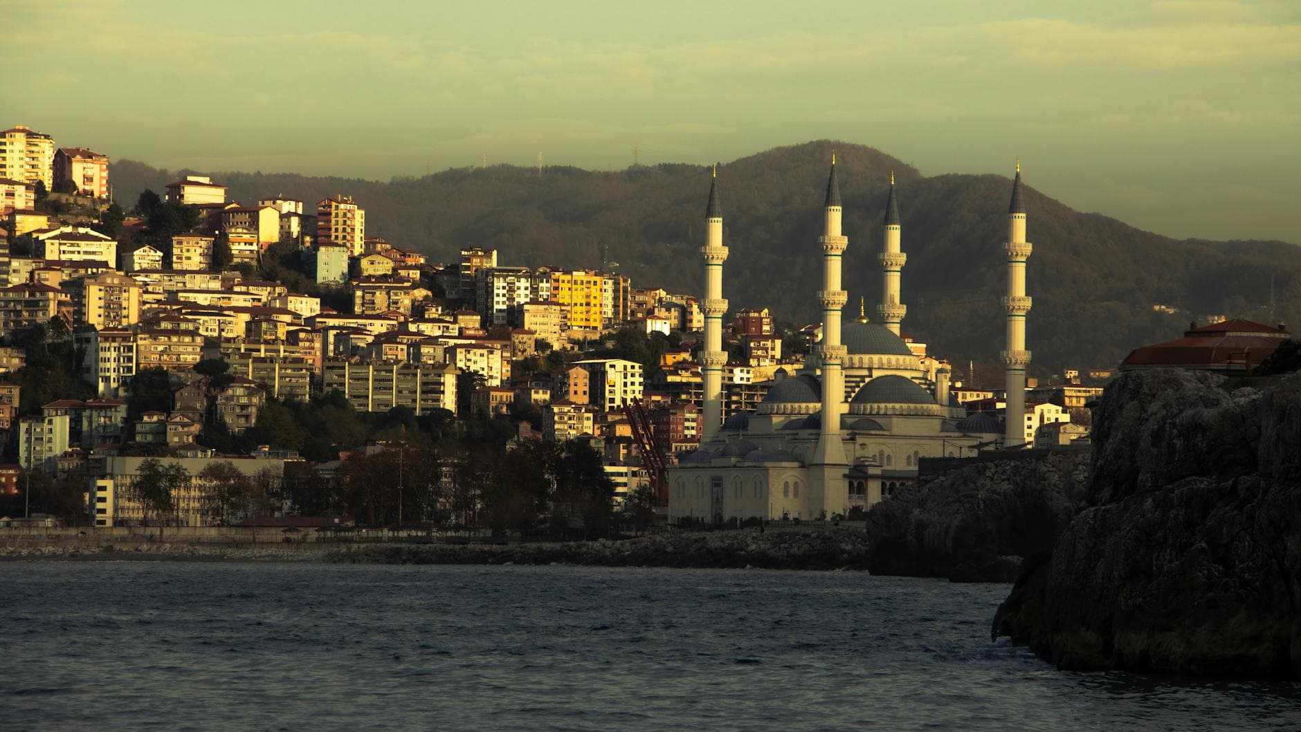 Scenic view of Zonguldak coastline with a mosque at sunset, against a mountainous backdrop.