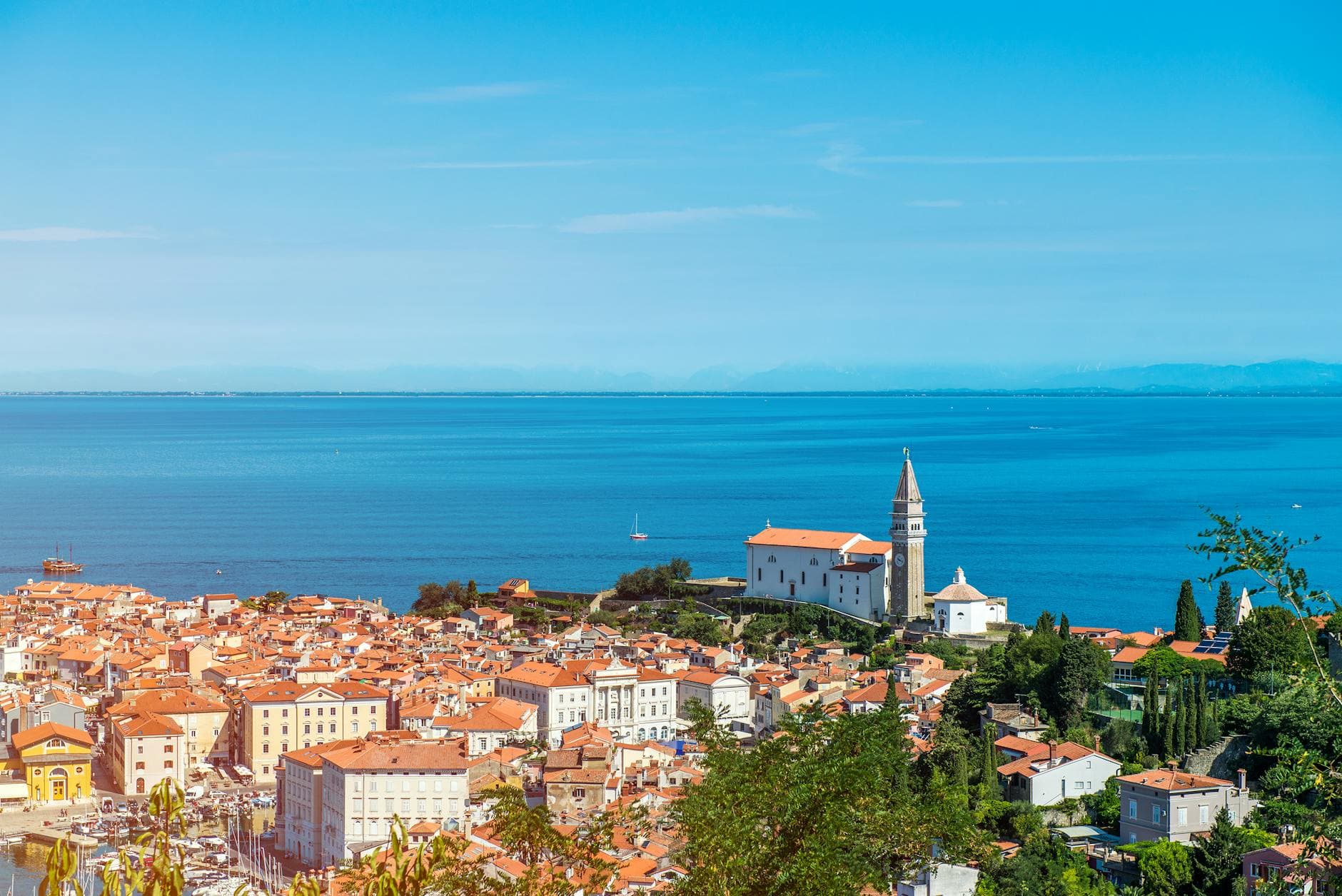 Scenic aerial view of a Mediterranean coastal town with a prominent church by the blue sea, under a clear sky.