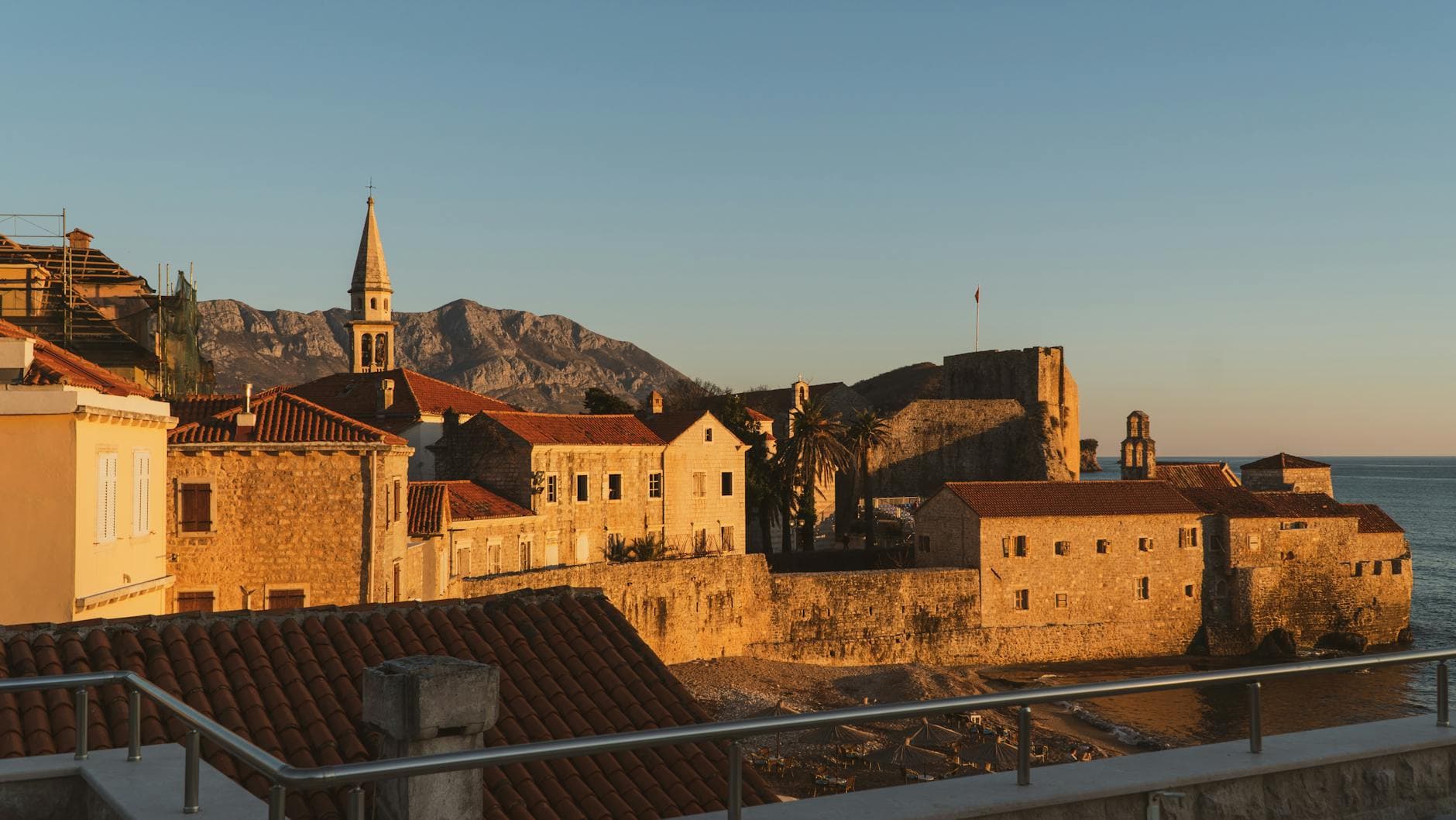 Scenic view of a historic Mediterranean coastal town with castle and sea at sunset.