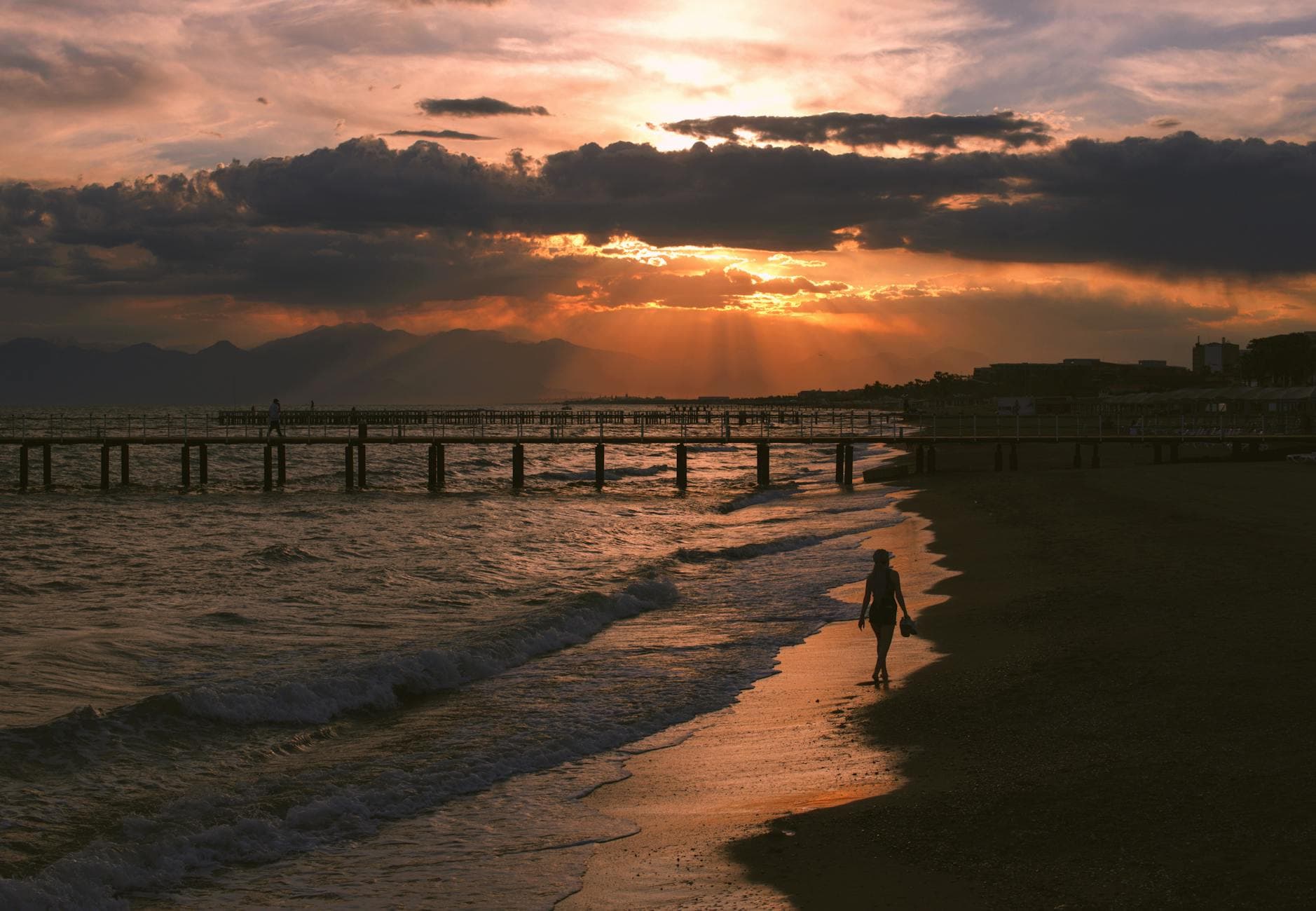 A serene sunset view over Belek beach in Antalya, Turkey, capturing the silhouette of a person walking along the shore.