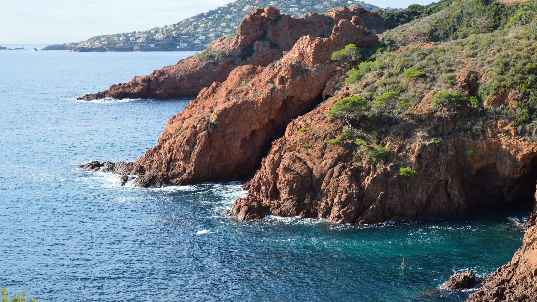 A breathtaking view of a coastal cliff with orange rocks and blue sea under daylight.
