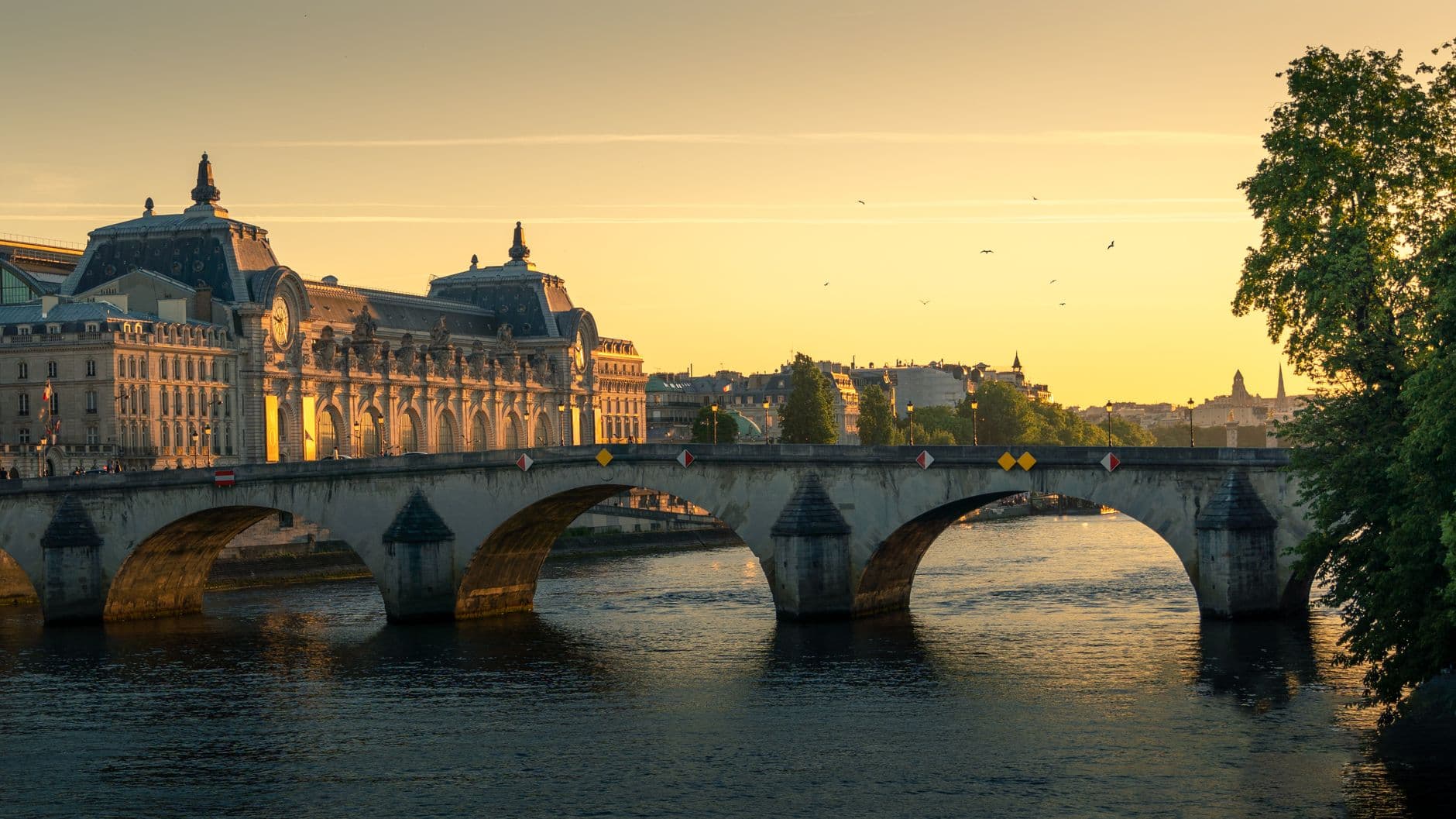 Scenic view of a historic arch bridge in Paris at sunset, showcasing the Seine River with the Musée d'Orsay in the background.