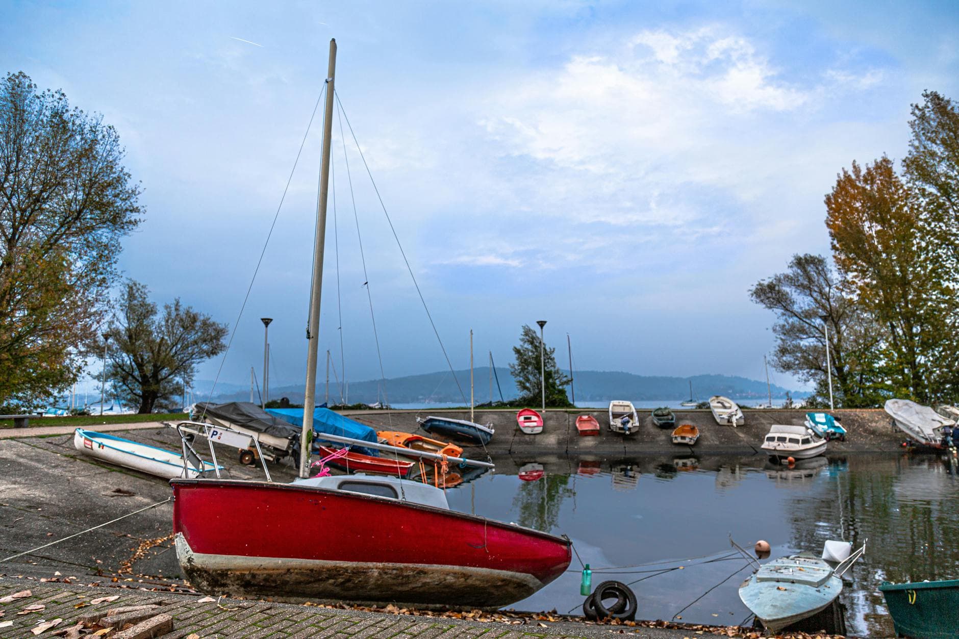 Serene view of small boats docked on Lake Maggiore's shore in Arona, Italy, during a cloudy day.