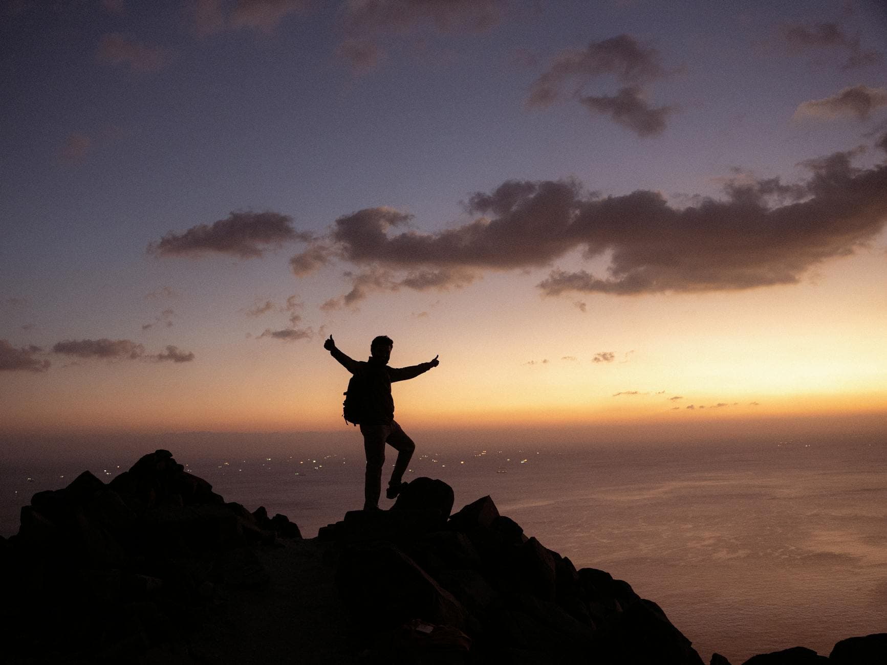 Silhouette of a hiker on a mountain ridge at sunset, overlooking the Gulf of Oman from Khor Fakkan, UAE.