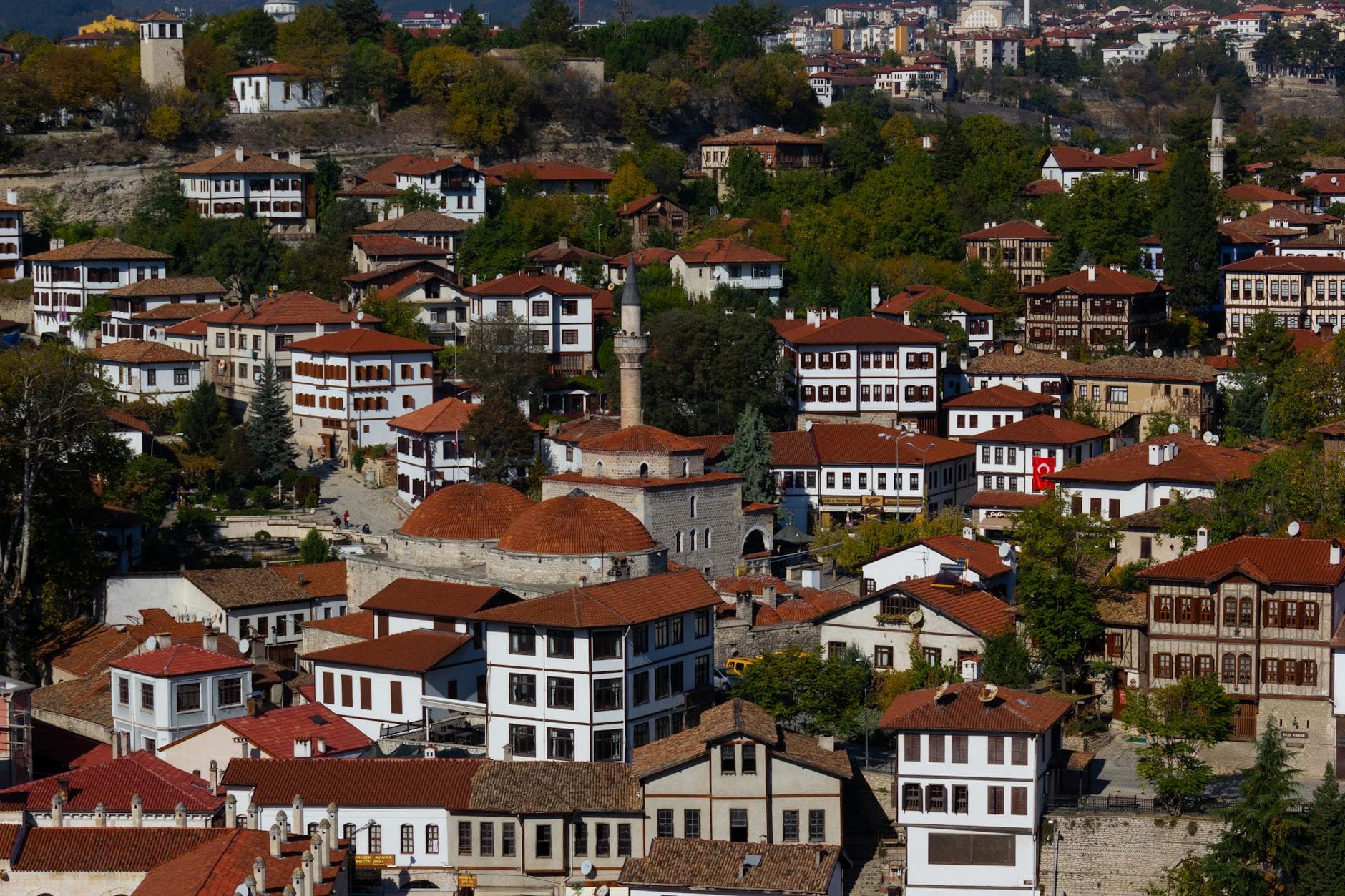 Aerial view of the historic Ottoman architecture in Safranbolu, Turkey, showcasing red-tiled roofs and vibrant greenery.