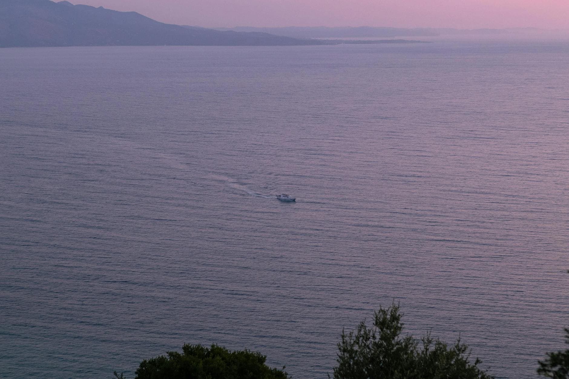 Serene view of the Ionian Sea at sunset with a distant boat and coastal mountains in Sarandë, Albania.