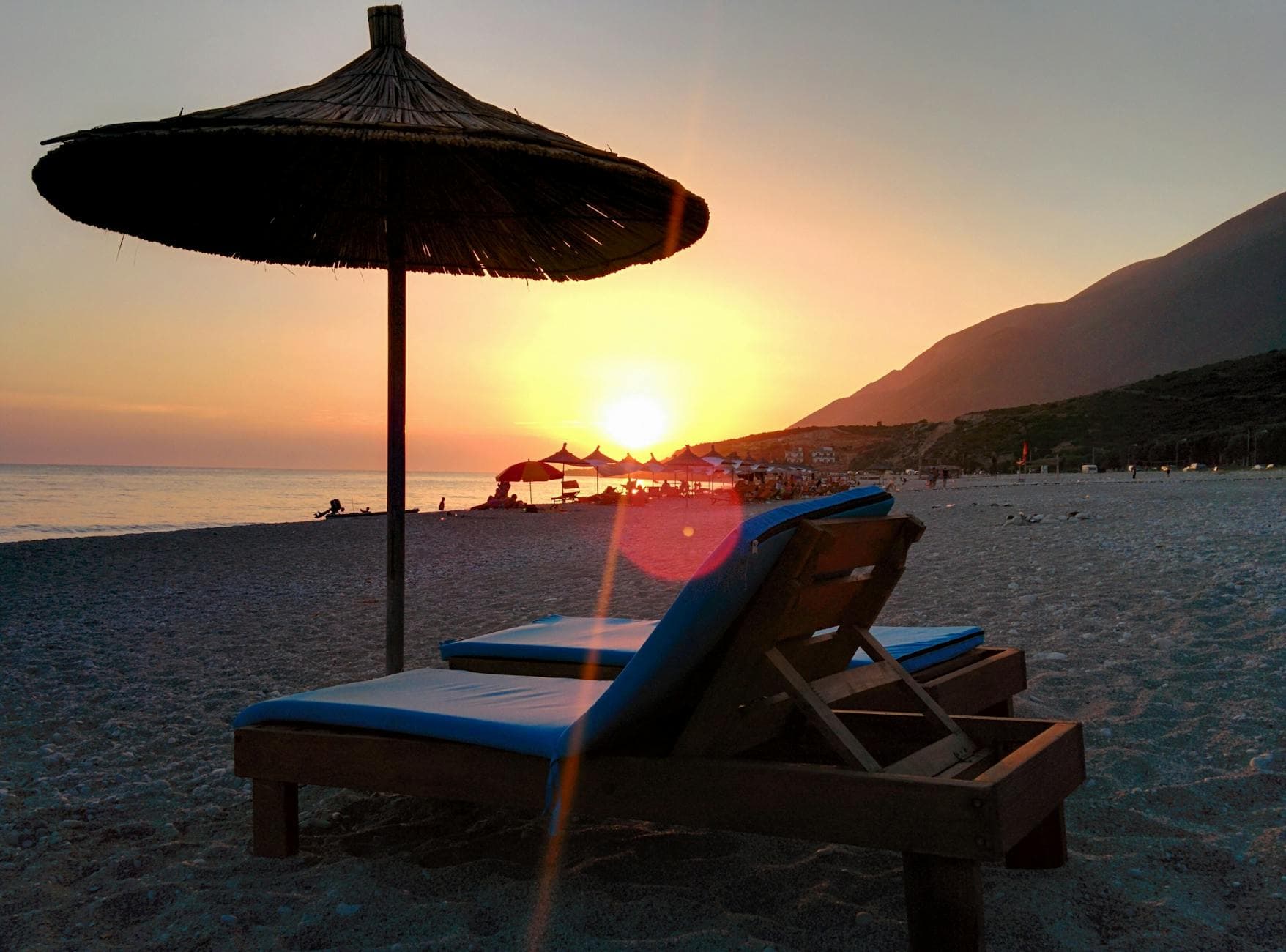 Relaxing sunset view on an Albanian beach with lounge chairs and straw umbrellas.