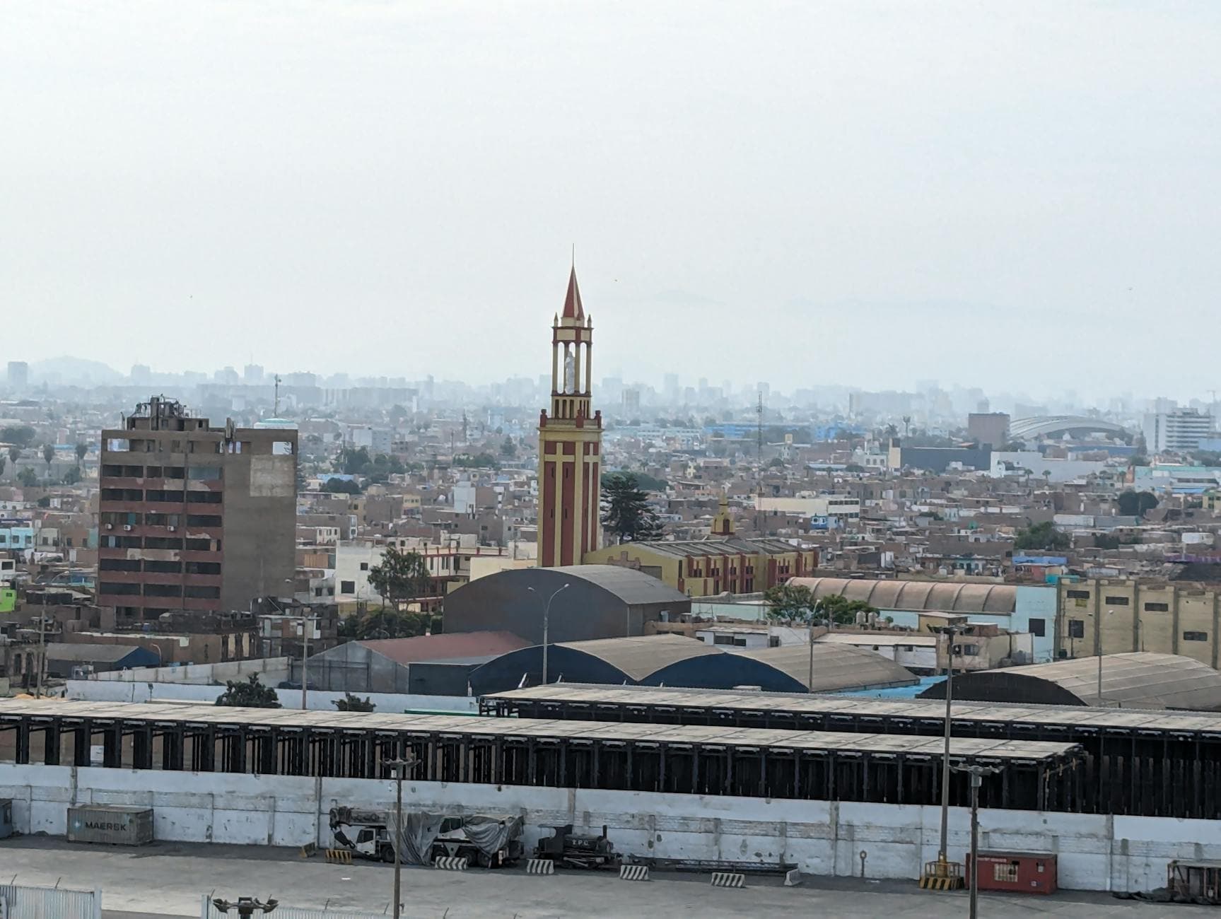 Urban cityscape with a prominent historic clock tower amidst a sprawling city skyline, overcast sky.