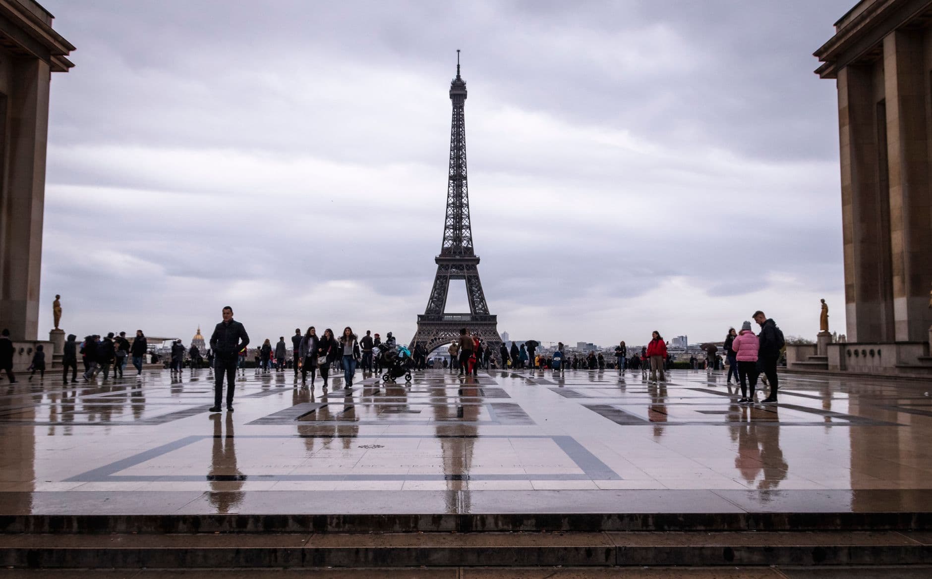 Tourists exploring Trocadéro Square with a stunning Eiffel Tower view on a cloudy day in Paris.