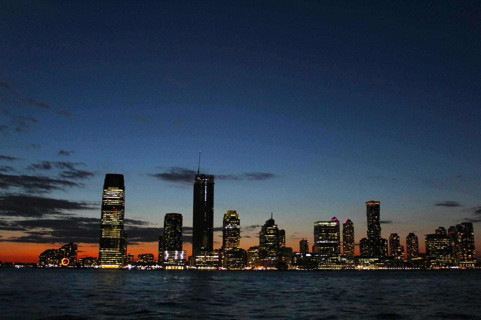 Beautiful city skyline with illuminated skyscrapers reflecting on the waterfront at dusk.